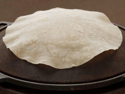 Soft-lit 3D render illustration of a large translucent Sonoran sobaquera flour tortilla over a domed iron griddle